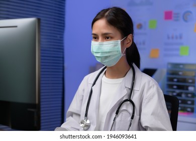 The Doctor Wearing Mask Is Sitting At A Desk At The Night, Working On Computer With Researching How To Treat The Patient's Condition.