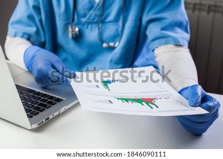 Doctor wearing protective gloves analyzing COVID-19 info data,sitting at office desk with a laptop,Coronavirus global pandemic crisis,medical scientific research showing number of cases  virus spread