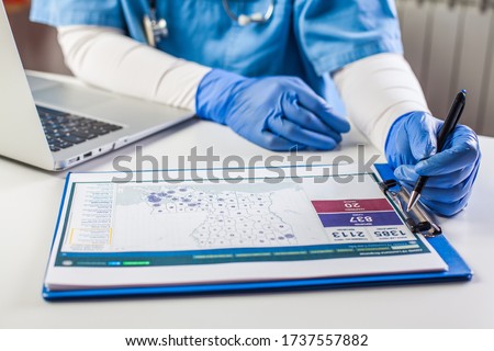 Doctor wearing protective gloves working on laptop computer,analyzing Coronavirus info data,COVID-19 response case info,U.S. state rank cases per capita,percent infected info and population numbers Stok fotoğraf © 