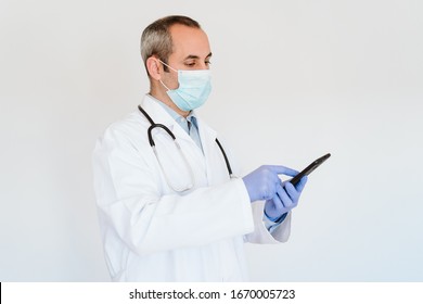 Doctor Wearing Protective Mask And Gloves Indoors Using Mobile Phone. Corona Virus Concept