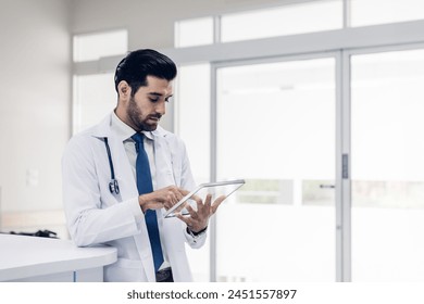 Doctor Wearing Scrubs In Hospital Corridor Using Digital Tablet. Doctor holding digital tablet. Confident male Medical Doctor Using Digital Tablet Computer. Health Care  Physician in White Lab Coat  - Powered by Shutterstock