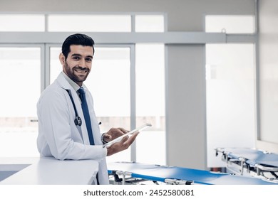 Doctor Wearing Scrubs In Hospital Corridor Using Digital Tablet. Doctor holding digital tablet. Confident male Medical Doctor Using Digital Tablet Computer. Health Care  Physician in White Lab Coat  - Powered by Shutterstock