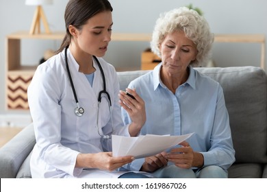 Doctor Wearing Uniform With Stethoscope Reading And Holding Documents, Consulting Older Woman About Checkup Result, Sitting On Couch, Mature Patient Listening To Physician Explaining Prescription