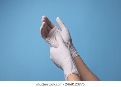 Doctor wearing white medical gloves on light blue background, closeup - Powered by Shutterstock