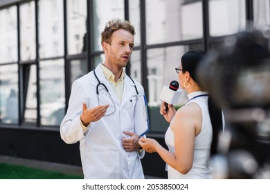 Doctor In White Coat Gesturing While Giving Interview To Asian Journalist With Microphone