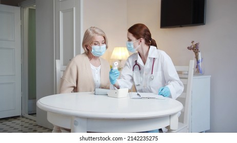 A Doctor In A White Coat Puts A Thermometer On The Patient's Forehead And Shows Her The Results