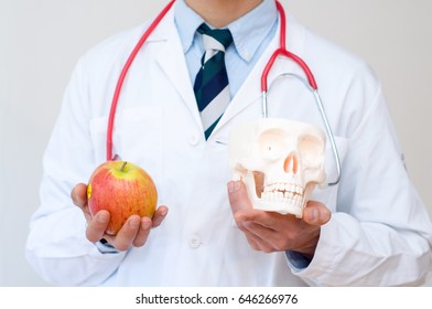 Doctor in white coat, with skull and apple in his hand - Shutterstock ID 646266976