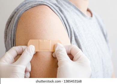 Doctor in white rubber protective gloves putting adhesive bandage on young man's arm after scratch on skin or injection of vaccine. First aid. Medical, pharmacy and healthcare concept. Closeup. - Powered by Shutterstock