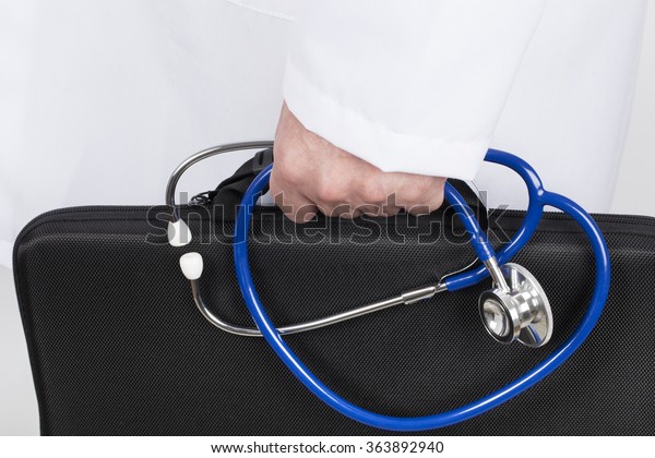 Doctor in white tunic holding black briefcase and stethoscope in his hand. He goes on a visit of his patients.