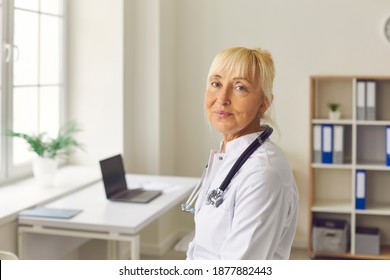 Doctor Who Does Not Lose Hope. Close Up Portrait Of Senior Tired Female Doctor Looking At Camera While Standing In Medical Office. Concept Of Medical Fatigue And Tiredness.