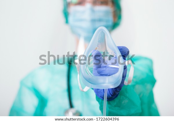 Doctor Woman holds Oxygen Mask for Inhale\
breath problem Patient, Coronavirus or Covid-19 attack Lungs.\
Healthcare worker in protective equipment put on oxygen mask\
patient diagnosis of\
coronavirus