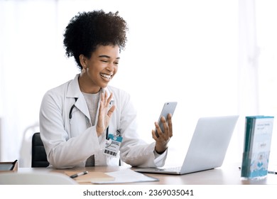 Doctor, woman and video call or phone communication in healthcare, social media or telehealth service at office. Happy african person or medical worker wave hello or talking on mobile voip for advice