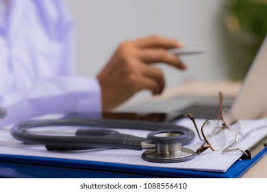 Doctor Work On Laptop Computer  With Clipboard, Stethoscope And Eye Glasses On The Table. Telemedicine, Teleconference, Ehealth, Online Medical Concept.