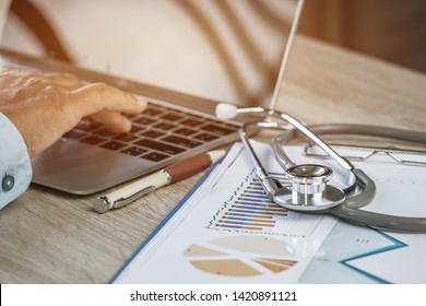 Doctor Working In Hospital Writing Prescription Clipboard, Working An Laptop On Desk In Hospital With Report Analysis, Healthcare Costs And Fees In Medical Hostpital Office