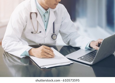 Doctor Working With Laptop Computer And Writing On Paperwork In The Hospital.