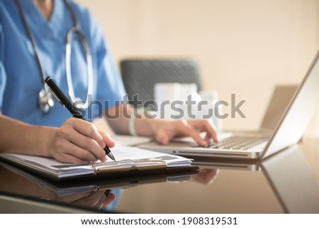 Doctor working with laptop computer and writing on paperwork.
