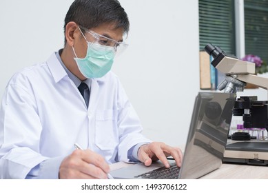 Doctor Working On Laptop Computer, Reviewing Lab Test. Technician Recording Laboratory Result On Laptop In Laboratory  With Microscope. Microbiology Investigation Concept