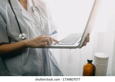 Doctor Working On Laptop Computer, Reviewing Lab Test. Technician Recording Laboratory Result On Laptop In Laboratory With Microscope. Microbiology Investigation Concept