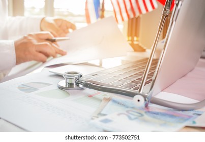 Doctor Working On Laptop Computer With Report Analysis And Money About Healthcare Costs And Fees In Medical Hostpital Office. Focus Stethoscope On Table. Healthcare Budget And Business Concept