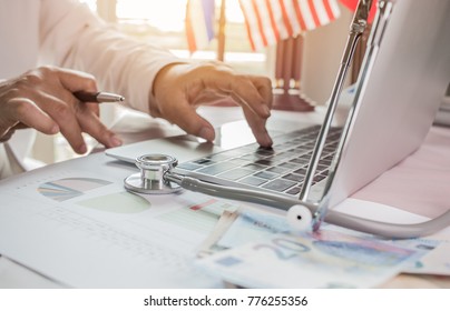 Doctor Working On Laptop Computer With Report Analysis And Money About Healthcare Costs And Fees In Medical Hostpital Office. Focus Stethoscope On Table. Healthcare Budget And Business Concept