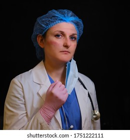 A Doctor With A Wounded Face Removes Mask After Working In The Hospital, Black Background. A Nurse In A White Coat And A Medical Beret With Marks On Her Face. Concept Stay Home, Coronavirus.