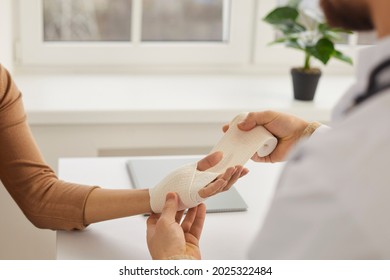 Doctor wrapping young woman's injured hand, close up. Doctor or nurse at modern medical office wrapping patient's sprained wrist with bandage. First aid and professional limb injury treatment concept