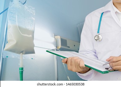 Doctor Writing Chart With Enteral Feeding Bag On IV Pole In Hospital Room Background.