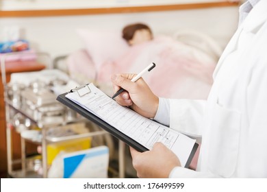 Doctor Writing On A Medical Chart With Patient. Fake Patient 