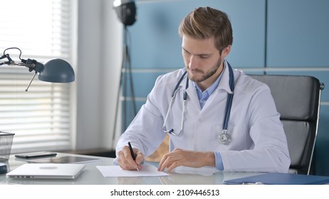 Doctor Writing On Paper While Sitting In Clinic 