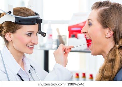 Doctor - Young Female Doctor Or ENT Specialist - With A Patient In Her Practice, Examining The Throat With A Spatula