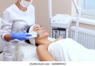 The doctor-cosmetologist makes the apparatus a procedure of ultrasound cleaning of the facial skin of a beautiful, young woman in a beauty salon. Cosmetology and professional skin care.