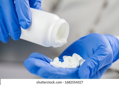 Doctor,nurse,GP medical practitioner wearing blue surgical latex gloves holding medicine bottle,taking out white pills,COVID-19 epidemic, Coronavirus virus disease global pandemic,cure trial concept - Shutterstock ID 1682554327