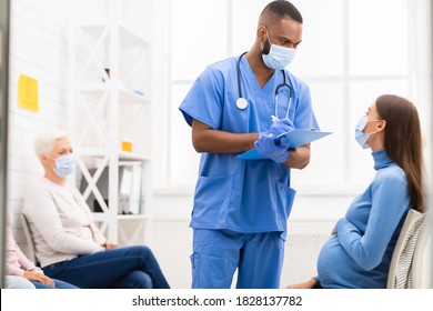 Doctor's Appointment During Coronavirus Pandemic. Male Nurse Talking With Pregnant Patient Woman In Hospital. Medical Treatment, Covid-19 Epidemic Concept. Selective Focus