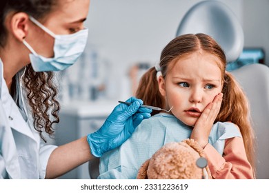 At the doctor's appointment. Portrait of a sad child sitting in a dentist's chair and holding a hand to his cheek from a toothache and looking away. Dental problems, discomfort. - Powered by Shutterstock