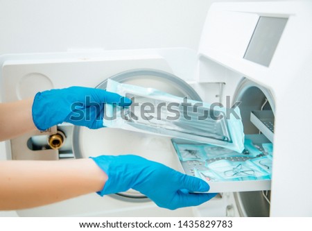 Doctor's assistant in blue gloves sterilize  dental steel set tools in autoclave. Hospital hygiene 