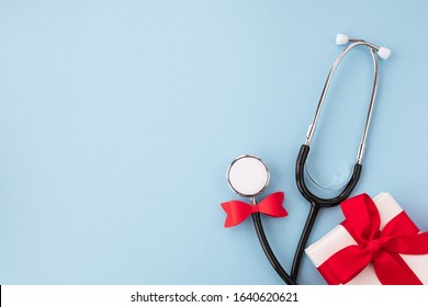 Doctor's day and World health day concept. Medical stethoscope in a festive red bow and gift on light blue background. Creative medical background, postcard. Top view, flat lay, copy space