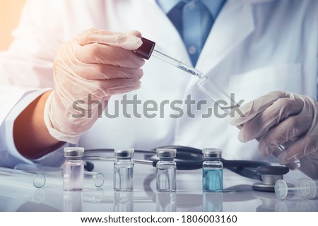 Doctors are dropping chemicals into a test tube to test an antiviral vaccine in the laboratory. Containing vials, vaccines, test tubes, syringes on a white table