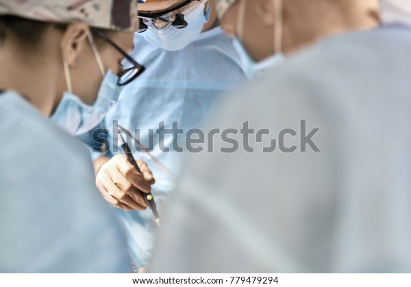 Doctors during the surgery in the operation\
room. They are wearing medical clothes and glasses. One of them is\
using a laser scalpel. Closeup.\
Horizontal.