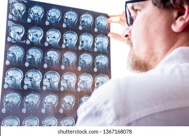 Doctors evaluation results of magnetic resonance imaging of brain in hospital concept photo. Neurologist in glasses keeps hand on glass of negatoscope MRI scan and examines structure of brain tissue 
