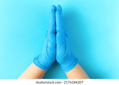 Doctor's Gloved Hands Folded Together On Blue Background. The Concept Of Prayer