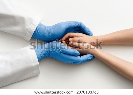 The doctor's gloved hands hold the child's hands. Medical concept.