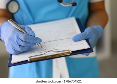 Doctor's gloved hands hold clipboard with pen and patient registration document. Patient registration and admission concept