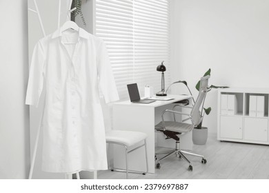 Doctor's gown on hanger near workplace in clinic