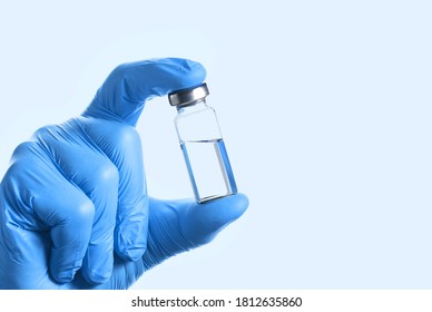 Doctor's Hand In Blue Gloves Hold The Vial With Vaccine Or Drug On Blue Background. Vaccination Concept.