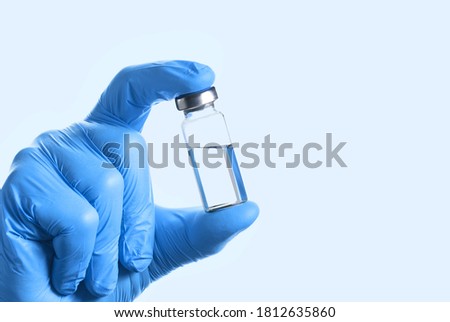 Doctor's Hand in blue gloves hold the vial with vaccine or drug on blue background. Vaccination concept.