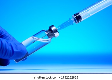 A doctor's hand in blue gloves picks up liquid from a vial into a syringe close-up on a blue background. Vaccine against covid-19. Insulin shot. Health care