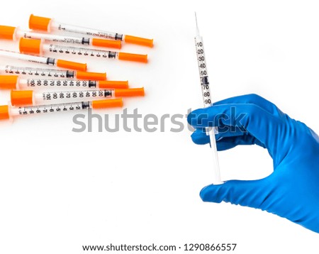 Doctor's hand in blue medical glove holding syringe with medical solution. Several empty syringes are nearby on white isolated background. Flu vaccine