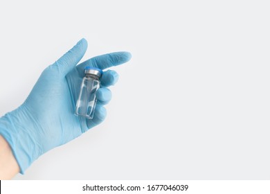 Doctors hand in blue rubber glove holding medicine bottle with blue cover and clear fluid on grey background. Coronavirus vaccine development. 2019-nCoV liquid drug, virus antidote. Copy space - Shutterstock ID 1677046039