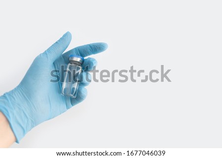 Doctors hand in blue rubber glove holding medicine bottle with blue cover and clear fluid on grey background. Coronavirus vaccine development. 2019-nCoV liquid drug, virus antidote. Copy space