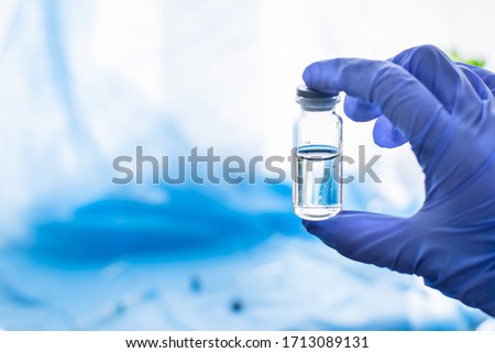 Doctor`s hand in glove hold glass medicine bottle with syringe injection on blue texture surgical sterile covering background. Coronavirus vaccine development of virus antidote.Copy space.Flat lay.